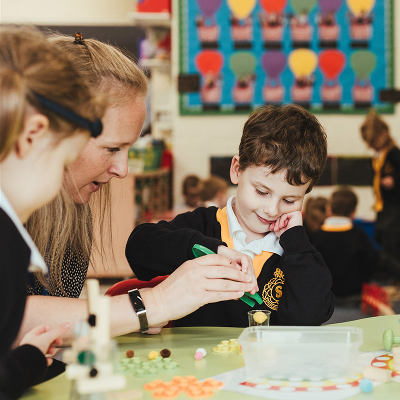 A teacher at Staplehurst School helping two students in early years with their work.