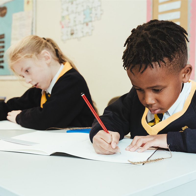 Two year 3 students at Staplehurst School writing in their sketchbooks in the classroom.